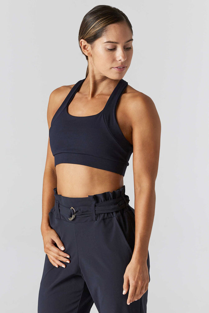 Woman wearing 9two5fit navy multi task racerback sports bra with spaghetti strap back details. Front-side view